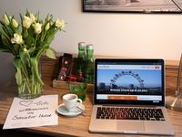 Senator Hotel Wien Tisch im Zimmer mit einem Laptop, einer Kaffeetasse, Blumen, zwei Wasserflaschen und einem Brief auf dem herzlich willkommen im Senator Hotel steht 