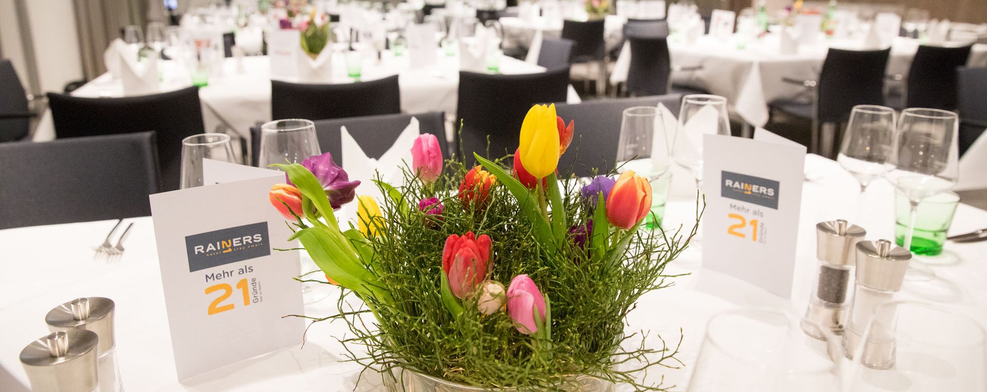 Blumenstrauß auf einem Tisch im Rainers21 Seminarraum mit voll gedeckten Tischen zur 60 Jahre Rainer Jubiläumsfeier