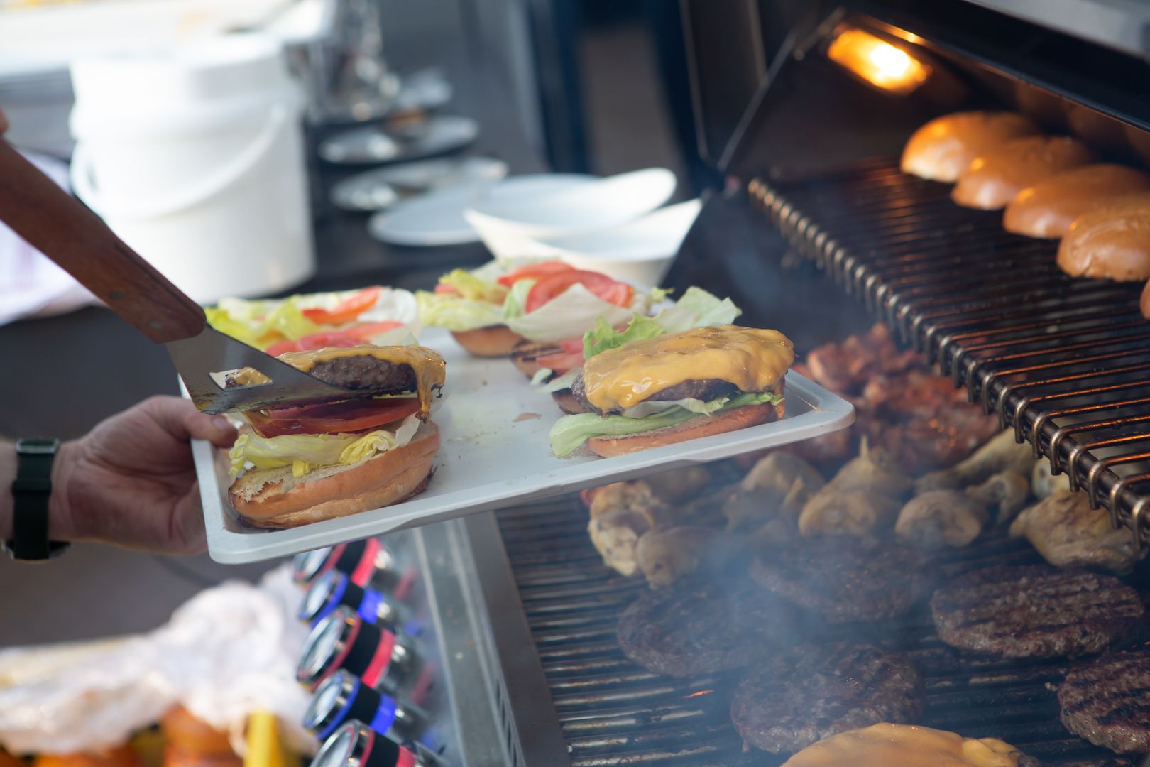 Ein Mann macht Burger die frisch vom Grill kommen auf der Rainers21 Seeterrasse